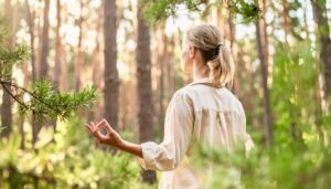 Eine junge, blonde Frau übt Yoga in einem Wald bei Sonnenuntergang und Waldduft. Warme Lichtstimmung.