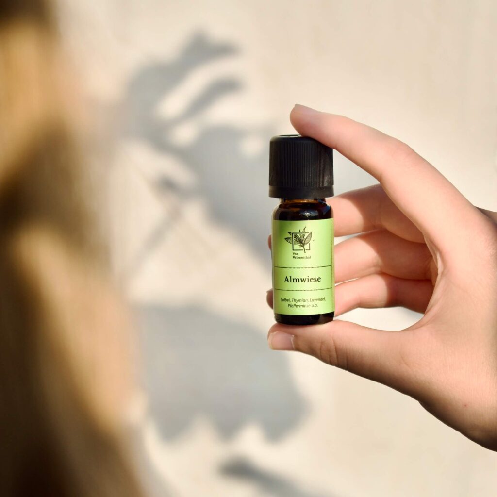 Eine Frau hält eine Flasche des Raumdufts Almwiese in die Sonne